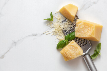 Poster - Parmesan cheese with basil leaves and iron grater on marble table top view, cooking background