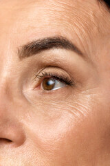 Cropped portrait of beautiful middle-aged woman eyes looking away over grey studio background. One eye.