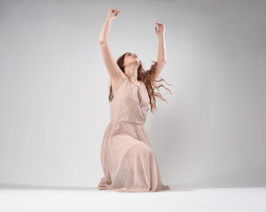 Canvas Print - Full length portrait of beautiful brunette model  wearing a  pink dress. graceful sitting  pose, kneeling on floor gestural hands. shot from low angle perspective,  isolated on white studio background