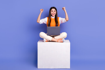 Sticker - Full length portrait of excited funky person sit podium raise fists use netbook isolated on purple color background