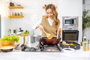 Wall Mural - Asian woman cooking healthy food fried pasta and salmon steak on cooking pan in the kitchen at home. Attractive girl preparing food for dinner party celebration meeting with friend on holiday vacation