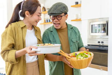Wall Mural - Asian couple enjoy and fun cooking food and salad together in the kitchen at home. People having dinner party meeting celebration holiday event eating food and drinking champagne together on vacation.