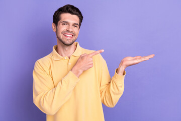 Poster - Photo of charming good mood guy wear yellow shirt holding arm pointing empty space isolated violet color background