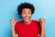 Closeup portrait of excited multiethnic youth student guy ecstatic winner raise fists wear red t-shirt isolated blue color background