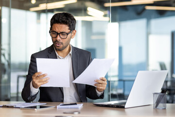 Upset financier investor checking accounts and contracts financial reports, businessman unhappy and disappointed with achievement results at workplace using laptop for paper work