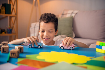 Wall Mural - Photo of cute sweet boy sit table after school homework have spare pastime playing driving toy cars in comfort apartment