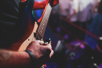 Wall Mural - Concert view of an electric guitar player with vocalist and rock band performing in a club, male musician guitarist on stage with audience in a crowded concert hall arena