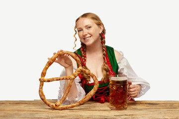 Wall Mural - Young redhead girl waitress, wearing a traditional Bavarian or German dirndl, serving big beer mugs with huge pretzel. Oktoberfest concept