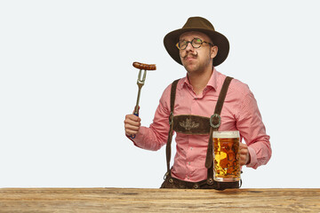 Wall Mural - Taste Oktoberfest. Delightful man wearing traditional fest Bavarian or German outfit with huge beer mug tasting fried sausage.