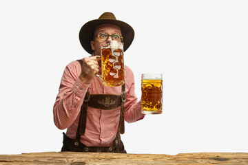 Wall Mural - Portrait of young cheerful man in hat, wearing folk Bavarian clothes, drinking beer isolated white background. Concept of Oktoberfest