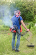 © Olena Vasylieva - Worker mowing tall grass with electric or petrol lawn trimmer in the backyard. it doesn't work properly.