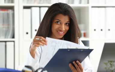 Wall Mural - Beautiful black smiling female doctor hold clipboard pad and fill something with silver pen. Physical illness prevention prescribe remedy ward round therapeutist assistance healthy lifestyle concept