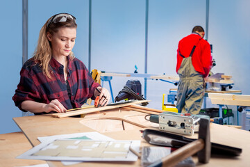 Poster - Woman works as carpenter. Girl in furniture workshop. Woman carpenter uses tape measure. Girl creates furniture for apartment. Female furniture factory worker. Carpenter work. Manufacturing business