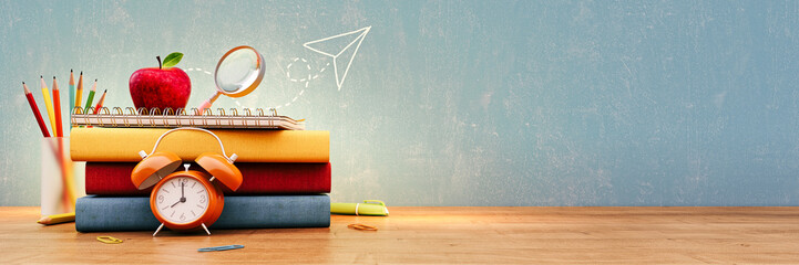 school books and school accessory on wooden table in front of empty blue chalkboard with copy space.