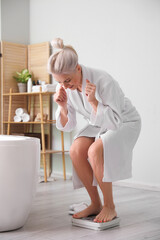 Poster - Mature woman measuring her weight on scales in bathroom