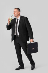 Poster - Mature businessman with glass of vegetable smoothie and briefcase on light background