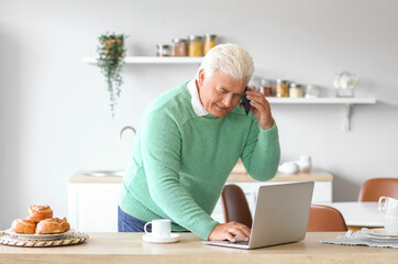 Sticker - Senior man with laptop talking by mobile phone in kitchen