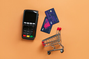 Wall Mural - Shopping cart with payment terminal and credit cards on beige background