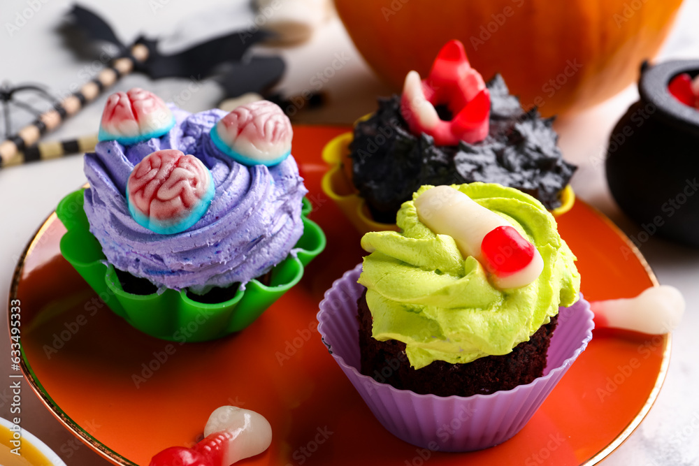 Plate with delicious Halloween cupcakes and candies on light background, closeup