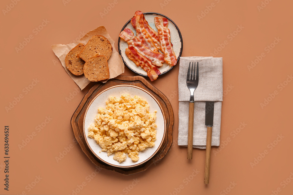 Plates of tasty scrambled eggs and bacon on brown background