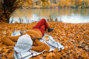 a young teenage girl is lying in a glade by the river bank in an autumn forest, enjoying the beautiful nature and bright yellow leaves