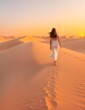frau läuft im sonnenaufgang sonnenuntergang über eine düne in einer wüste abudhabi sand sahara dubai 1001 nacht romantik schleier kleid sommer sommerkleid urlaub - fiktive person mit generativer ki
