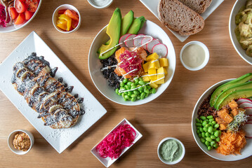  plates of delicious healthy organic food seen from above on wooden table with poke, , sauces, condiments , pancakes.