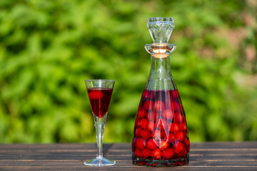 Homemade cherry brandy in glasses and in a bottle on a wooden table in a summer garden