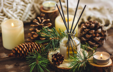 Christmas home aromatherapy. Aroma diffuser with pine extract, organic essential oil, cedar and spruce cone, candles on wooden table. Cozy atmosphere, holiday spirit. Winter inspiration and mood.