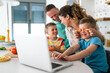 © Dorde - Smiling excited young parents entertaining their children while playing with carrots in the kitchen. Son is using laptop.