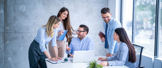 Group of business professionals gather around a desk engaging in a focused discussion holding notebooks and documents during meeting with their executive director at office.