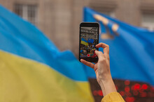 Ukrainians And Supporters Rally. Stand With Ukraine. Hand Shooting Video Of Demonstration On Mobile Phone Over Ukrainian And Crinean Tatar Flags Background. Close Up, Bokeh. Copy Space. Outdoor Shot