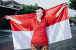 Happy smiling Indonesian woman wearing red kebaya holding Indonesia's flag to celebrate Indonesia Independence Day. Outdoor photoshoot concept