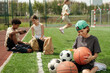 © pressmaster - Cute schoolboy looking at basketball ball in his hands while choosing item for playing sports game against intercultural classmates or friends
