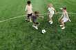 © pressmaster - Above view of four active kids in sportswear running along green football field while playing soccer together at stadium on weekend or at leisure