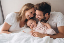 Multiracial Diverse Young Family Couple Playing With Cute Baby Child In Bed Holding Infant Kid Girl. Happy Multiethnic Parents Having Fun In The Morning Lifting Small Daughter In Bedroom At Home