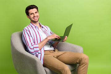 Poster - Photo of good mood man with stubble dressed striped shirt typing email on laptop sit in armchair isolated on green color background