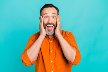 Wall Mural - Photo of shocked excited man dressed orange shirt arms cheeks open mouth isolated turquoise color background