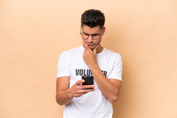 Wall Mural - Young volunteer caucasian man isolated on beige background thinking and sending a message