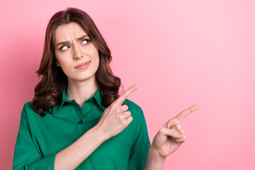 Sticker - Photo of pretty doubtful lady wear green shirt pointing two fingers looking empty space isolated pink color background