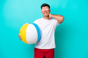 Wall Mural - Young caucasian man holding a beach ball isolated on blue background laughing