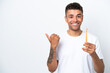 Young Brazilian man brushing teeth isolated on white background pointing to the side to present a product