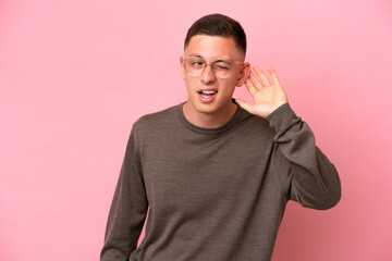 Wall Mural - Young Brazilian man isolated on pink background listening to something by putting hand on the ear