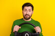 Photo of young guy nervous biting lips wear green stylish sweater driving steering wheel panic doubts isolated on yellow color background