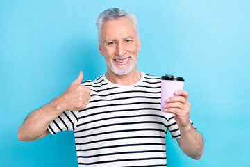 Poster - Photo of satisfied pensioner wear striped trendy clothes hand hold espresso thumb up delicious beverage isolated on blue color background