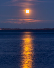 Wall Mural - Bright full moon glowing in a hazy night sky and reflecting in a calm body of water
