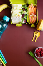 School Lunch Box With Sandwiches, Carrot Sticks, Apple, Banana, Lettuce, Hummus And Raspberries. Healthy School Lunch Concept. Burgundy Background. Top View. Place For Text