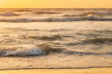 Wall Mural - Sea ocean water surface with foaming small waves at sunset. Evening sunlight sunshine above sea. Ocean water foam splashes washing sandy beach. Natural sunset sky warm colors. Amazing landscape