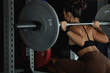 Back view, woman lifting weight, squatting with barbell in gym, sporty woman exercising 