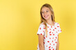 © Roquillo - blonde kid girl wearing polka dot shirt over yellow studio background very happy and excited about new plans.